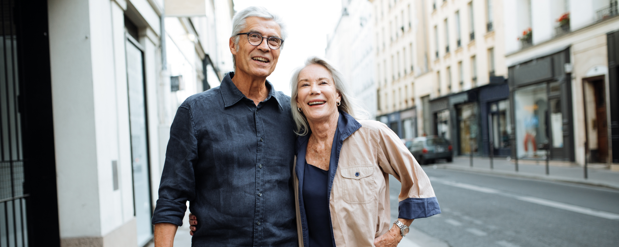 Man and Woman standing on the sidewalk of a city smiling and looking into the distance.