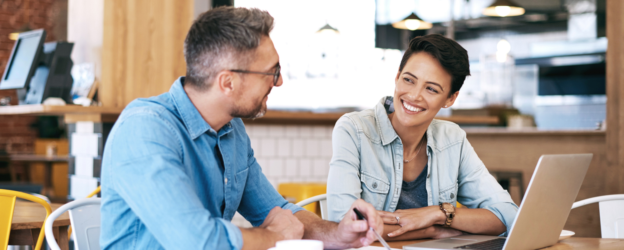 Woman smiling at a man while they have a laptop open at a cafe