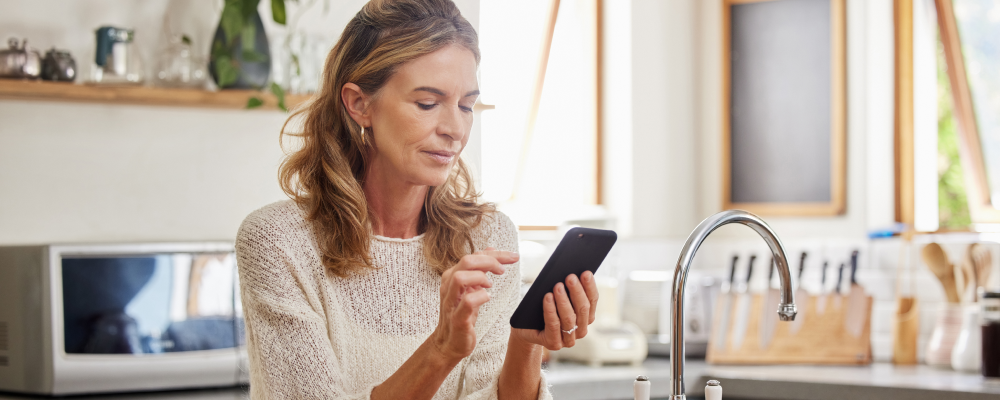 Woman looking at her phone from her sunny kitchen