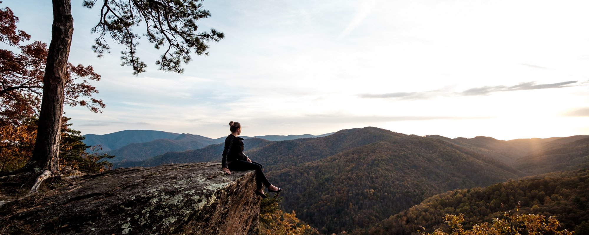 Woman sitting on a rock at the peak of a hike watching the sunset